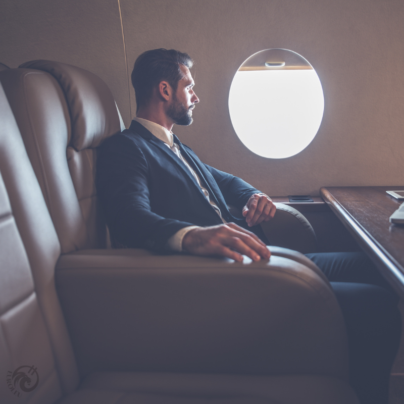 Antreprenor tânăr și elegant în costum bleumarin, așezat contemplativ într-un scaun de lux la bordul unui jet privat, privind pe geamul oval iluminat – imagine simbolică pentru succesul financiar, ambiție și mobilitate globală în lumea afacerilor românești, cu logo EuroLeu.com discret în colț.